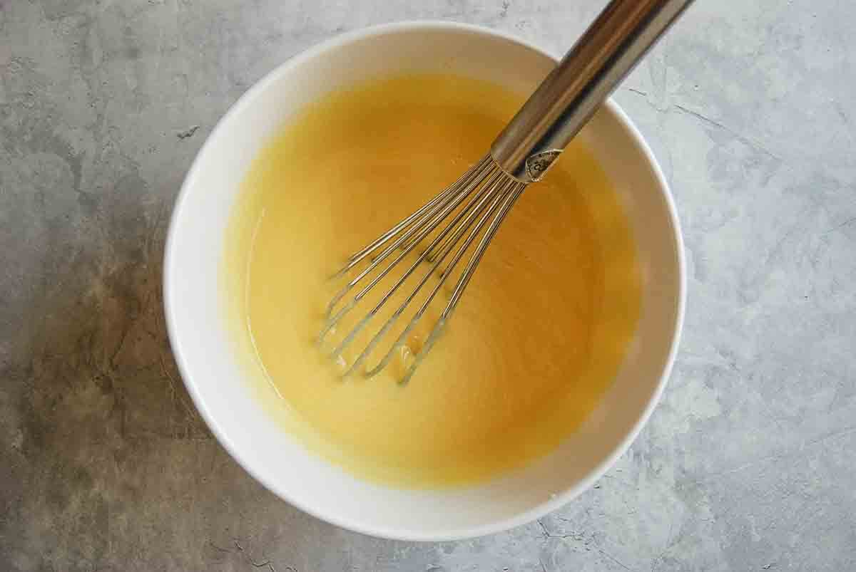 A metal whisk in a white bowl filled with a vanilla pudding.