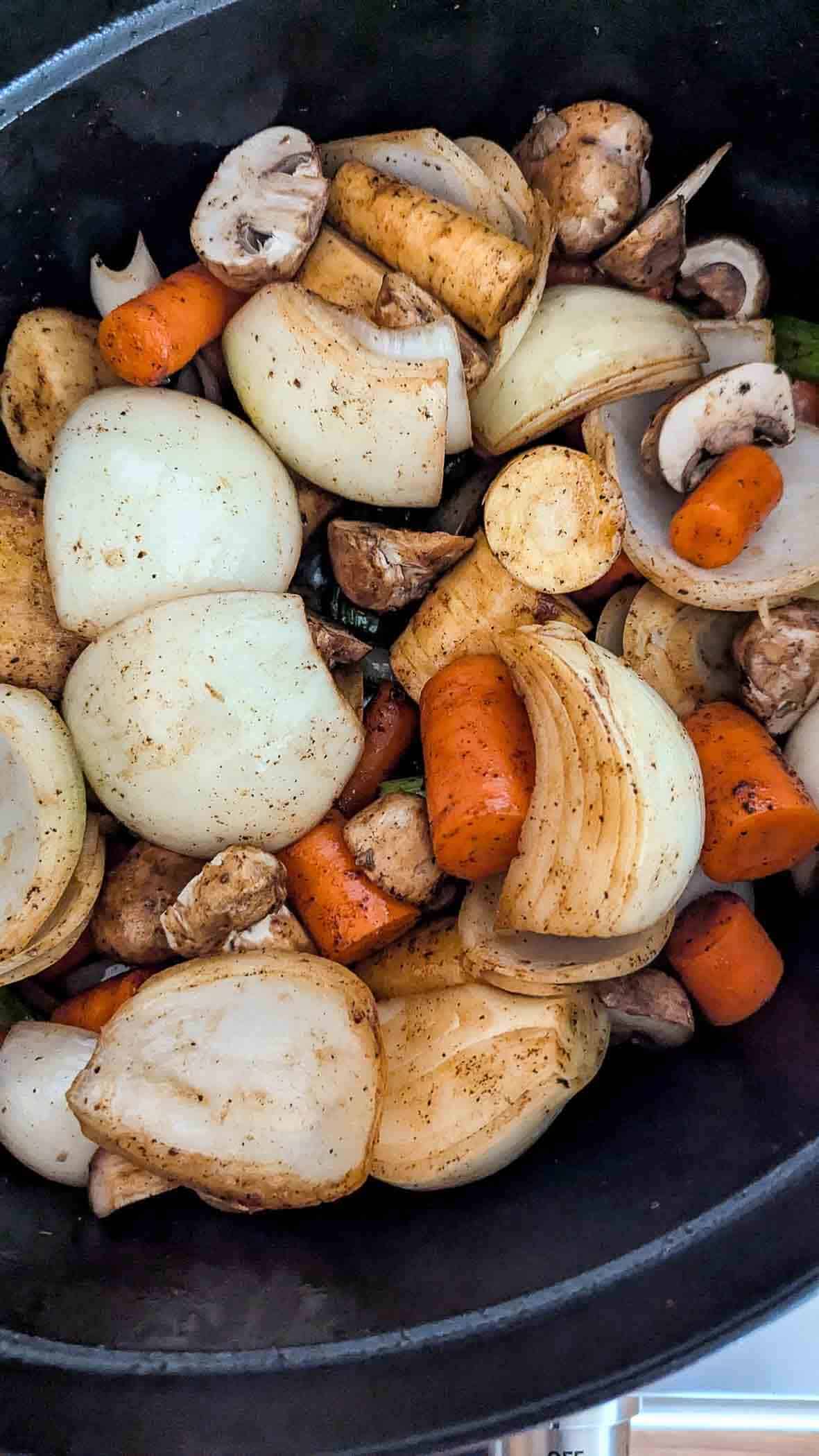 Chopped onions, carrots, mushrooms, and garlic seasoned with spices are piled in a dutch oven.
