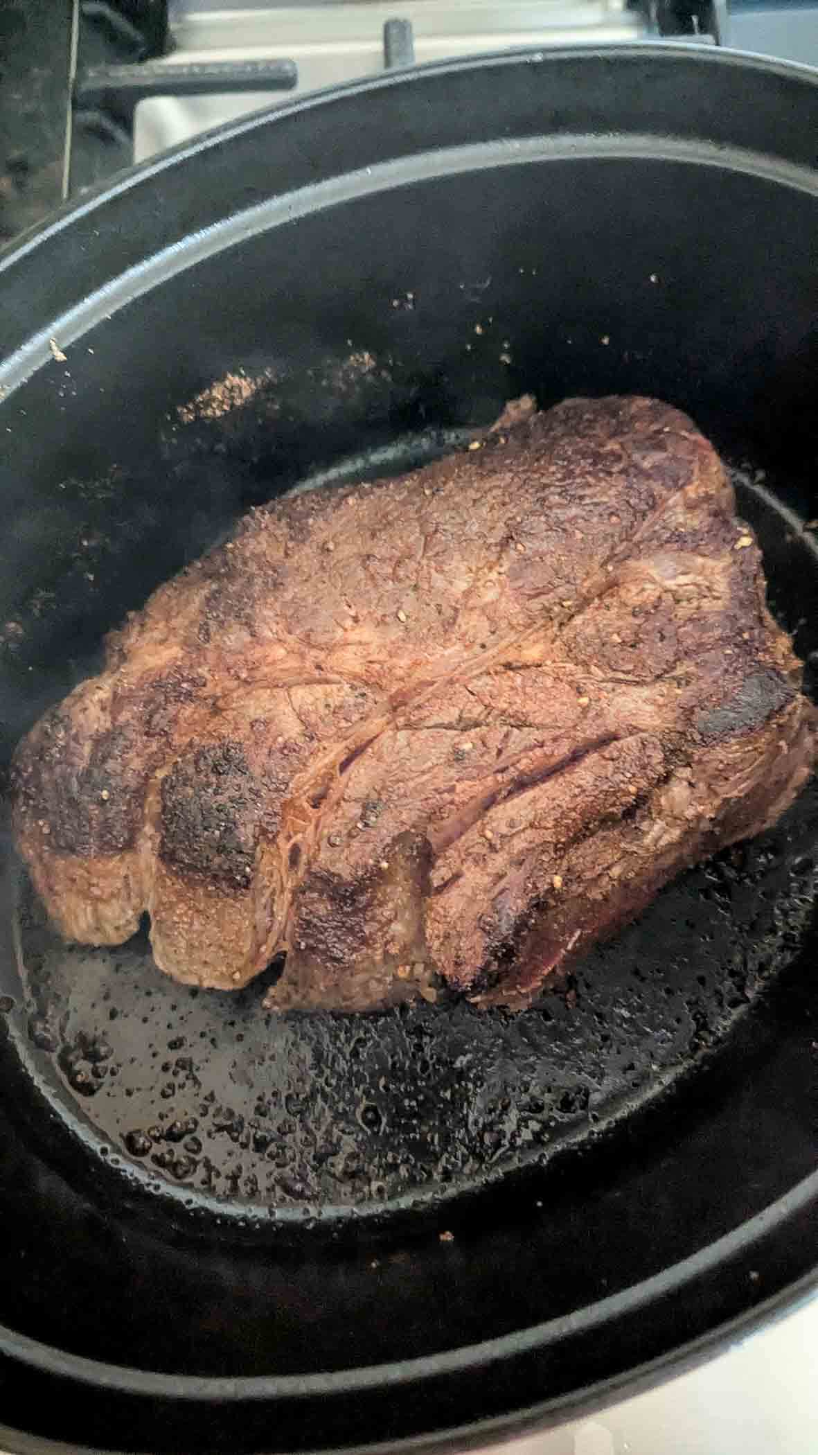 A large, seared beef roast sits in a dutch oven on a stove.