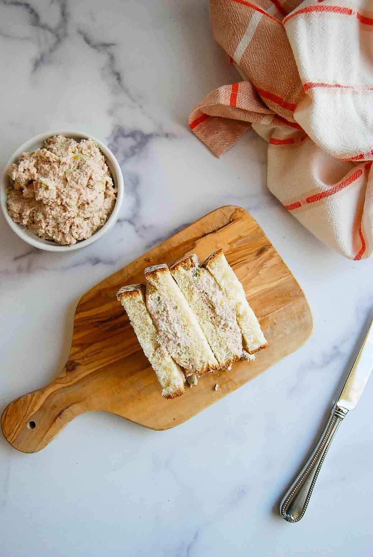 A wooden cutting board with four ham salad sandwiches.