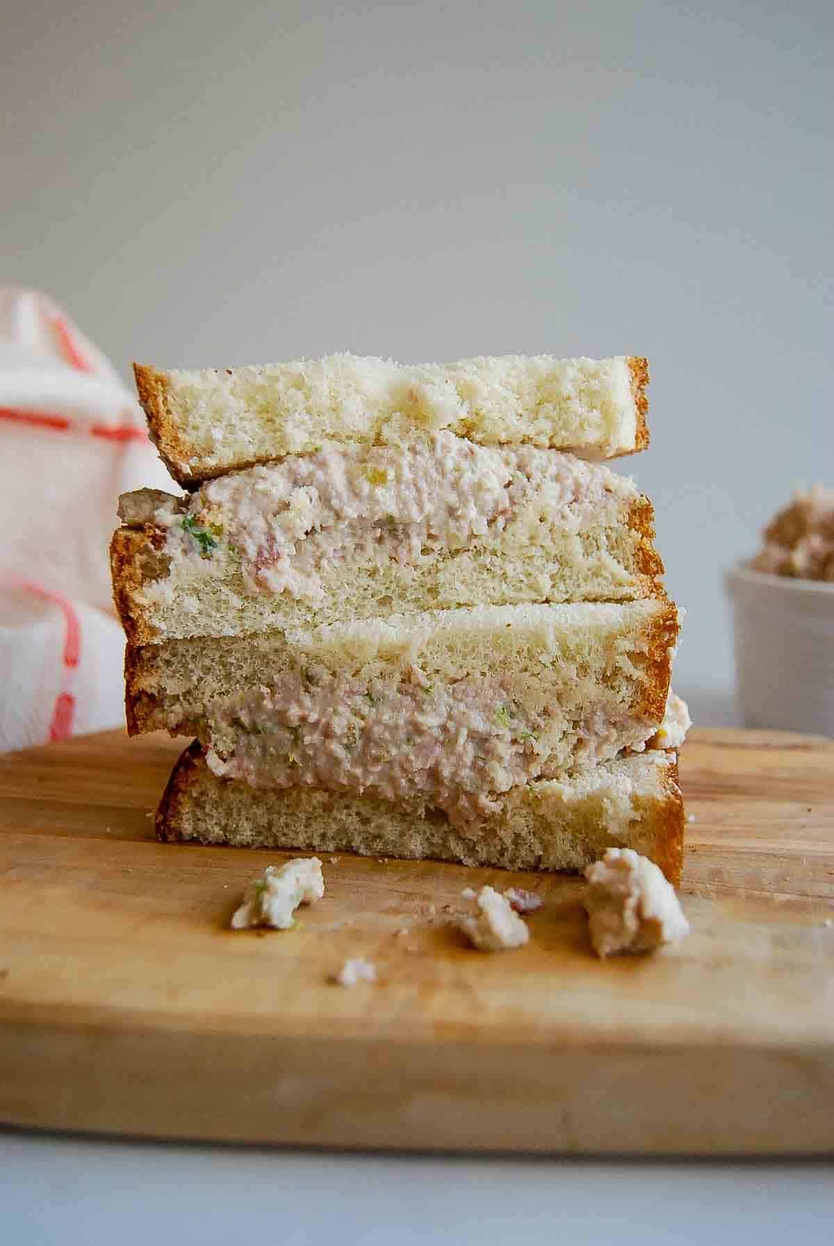 Two halves of a sandwich with a creamy ham salad filling, stacked on a wooden cutting board.