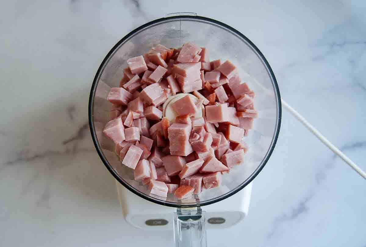 A food processor filled with evenly diced cubes of ham.