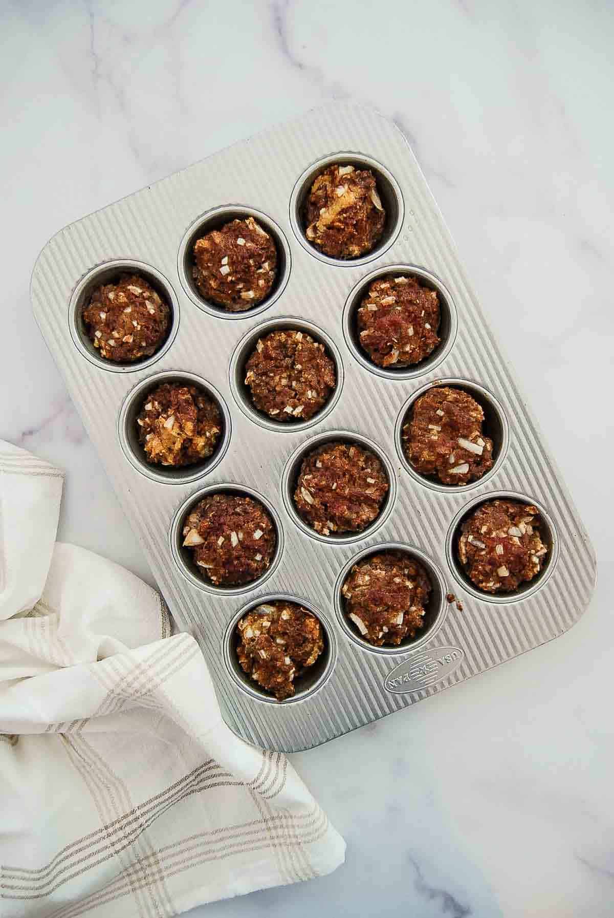 A muffin tin filled with twelve cooked mini meatloaf sits on a marble countertop.