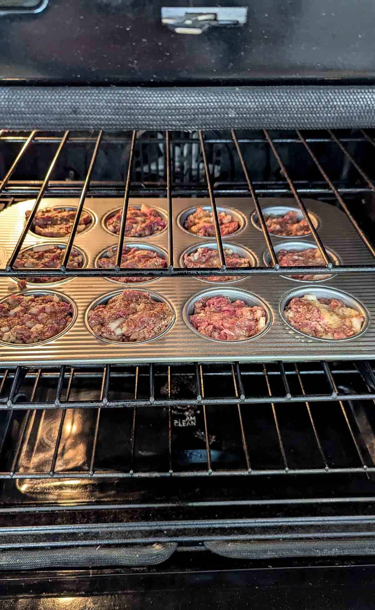 A muffin tin filled with unbaked mini meatloaves is placed on the middle rack inside an oven.