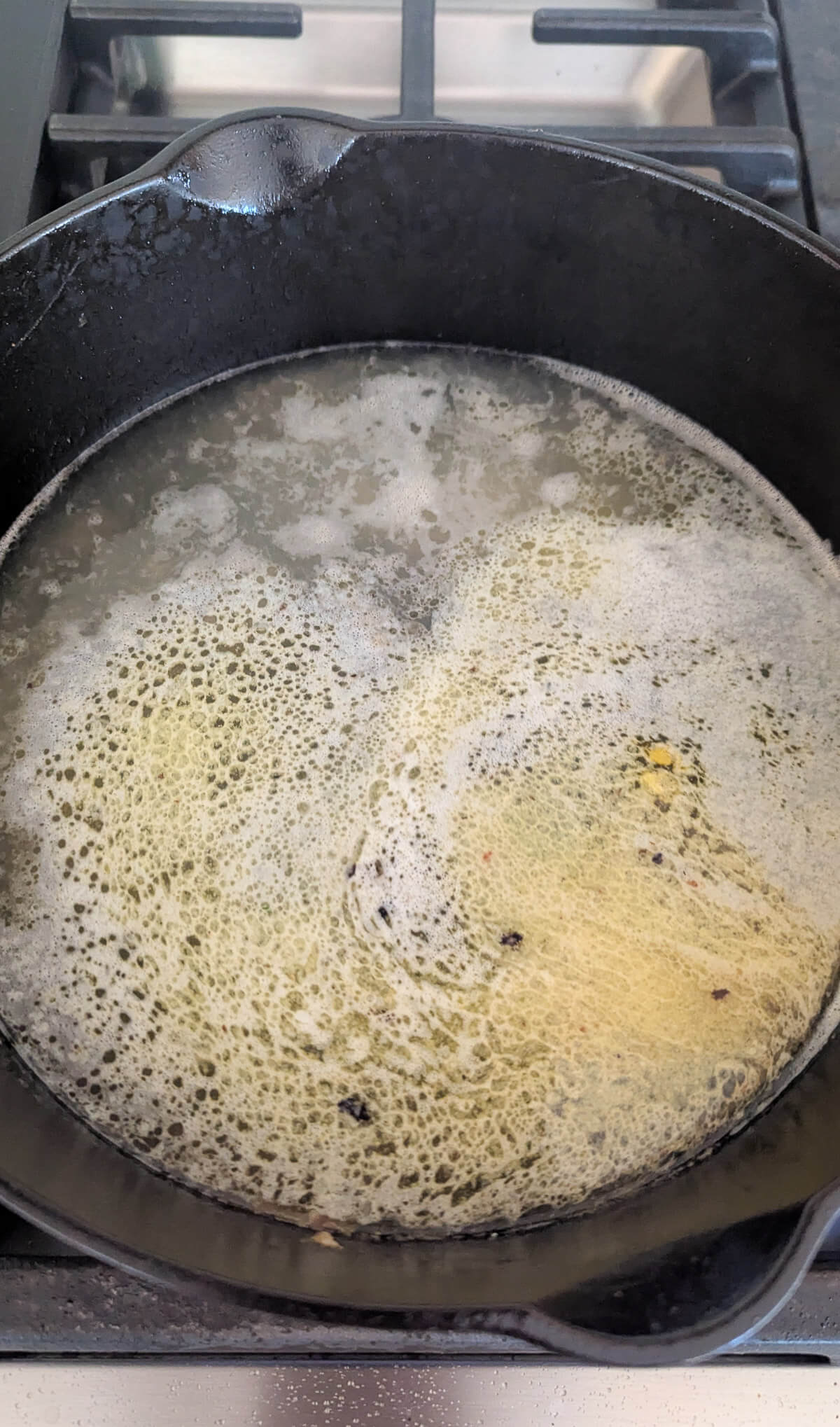 A cast iron skillet on a stovetop contains bubbling butter and wine mixture.