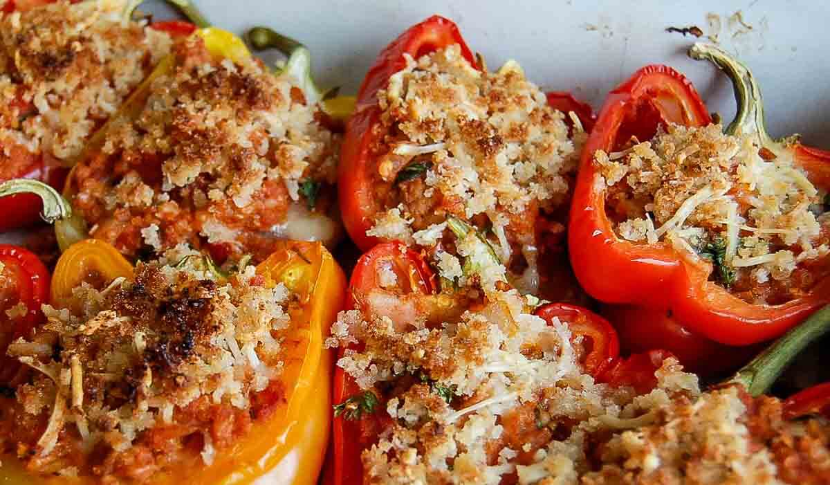 Close-up of ground turkey stuffed peppers topped with a golden-brown breadcrumb and cheese mixture, baked until crispy. The peppers are a mix of red and yellow, filled with a savory stuffing.