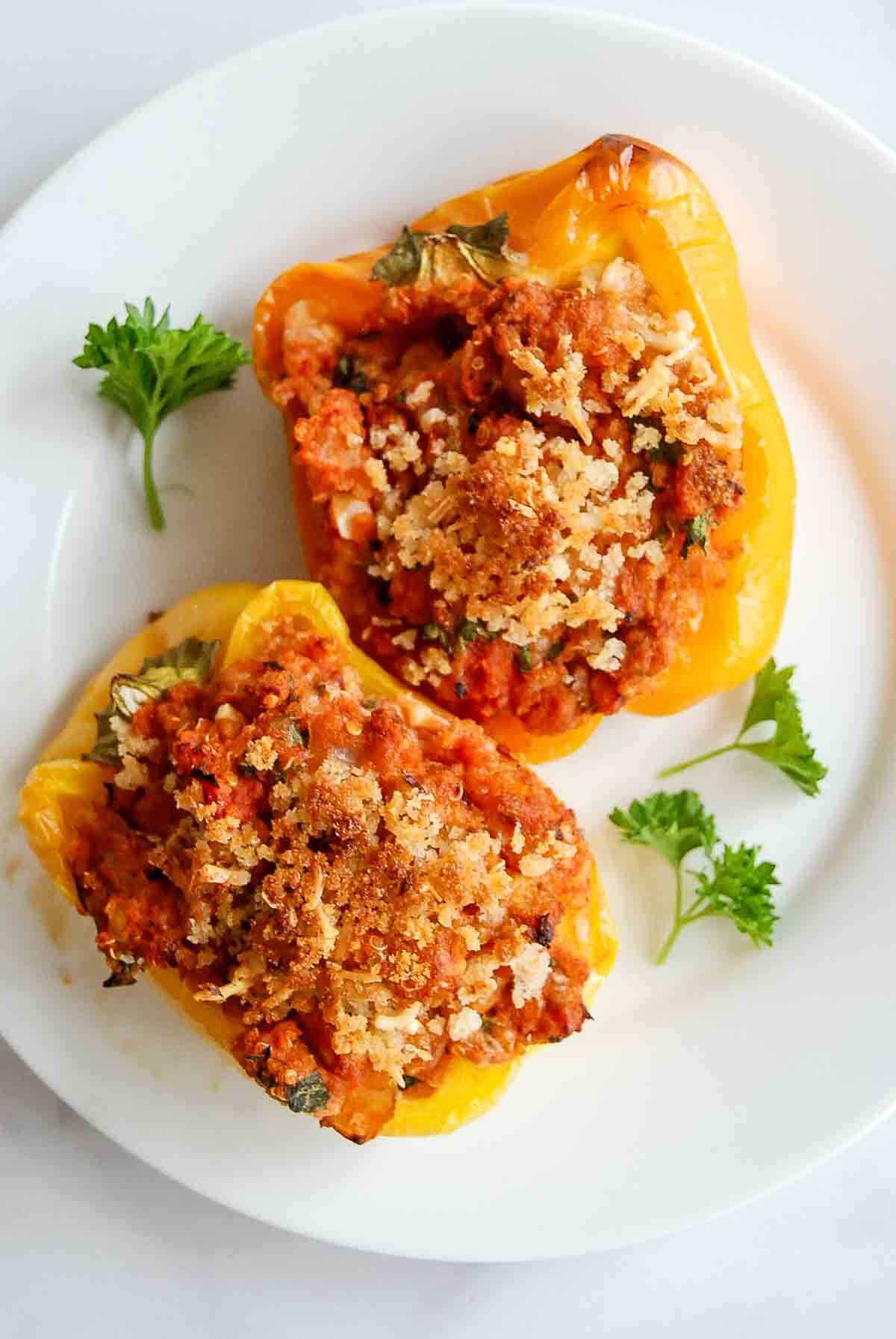 Two yellow bell pepper halves stuffed with a ground turkey, tomato-based filling and topped with crispy breadcrumbs, served on a white plate with fresh parsley garnishes.
