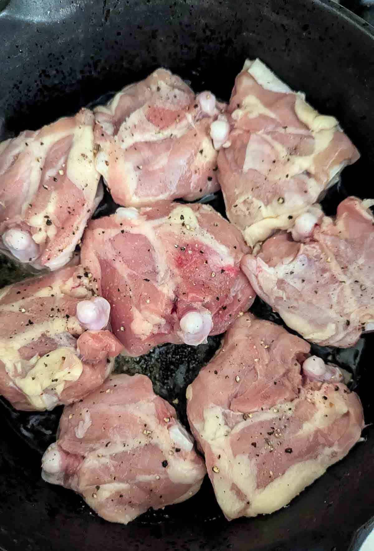 Raw, seasoned chicken thighs arranged in a black frying pan, ready to be cooked.