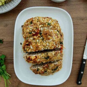 A loaf of homemade turkey meatloaf, partially sliced, sits on a white plate on a wooden table.
