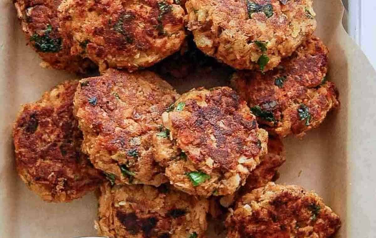 A tray lined with parchment paper holds several golden-brown, crispy salmon cakes.