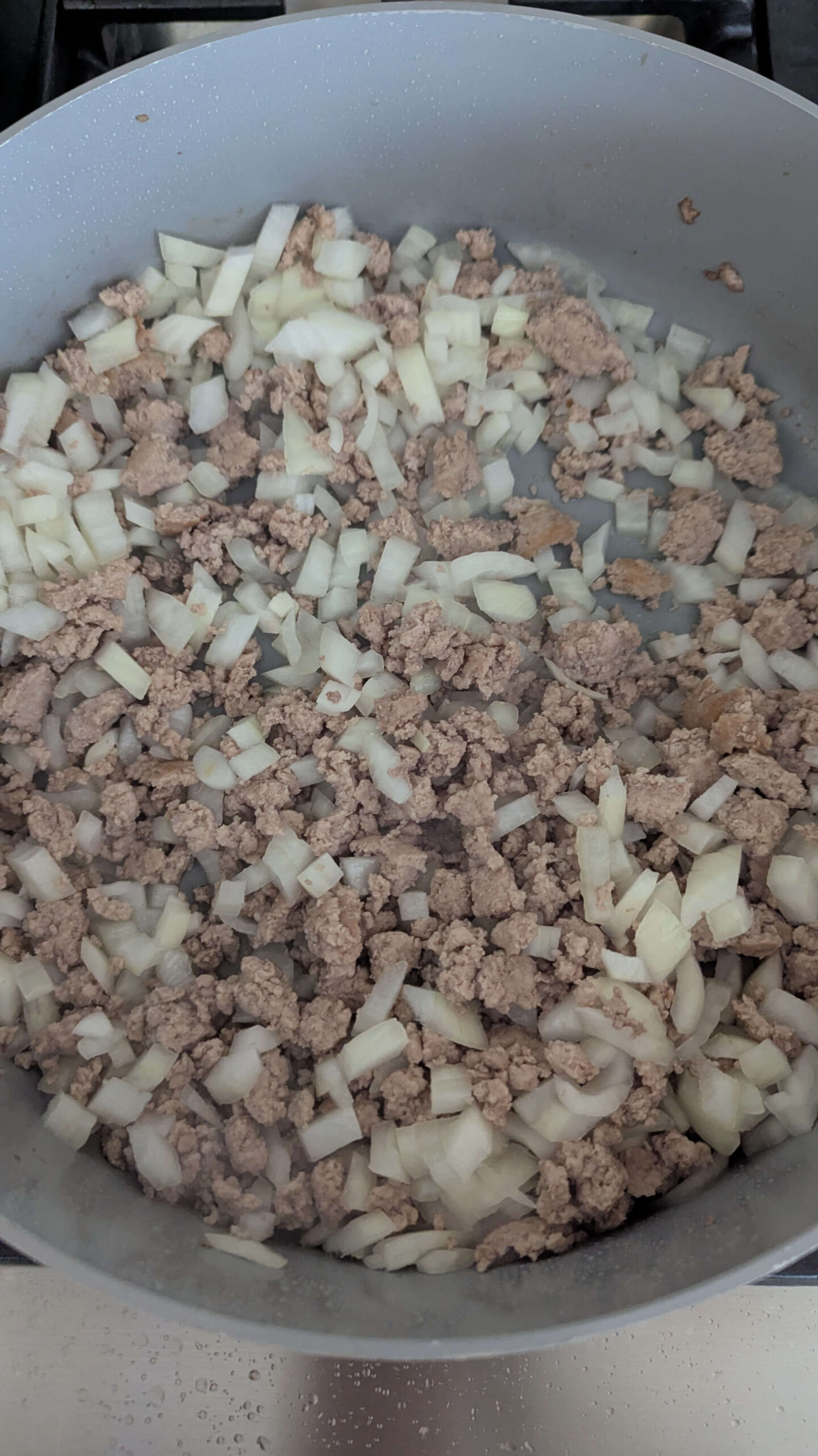 Ground turkey and chopped onions are being cooked together in a large pan on a stovetop.