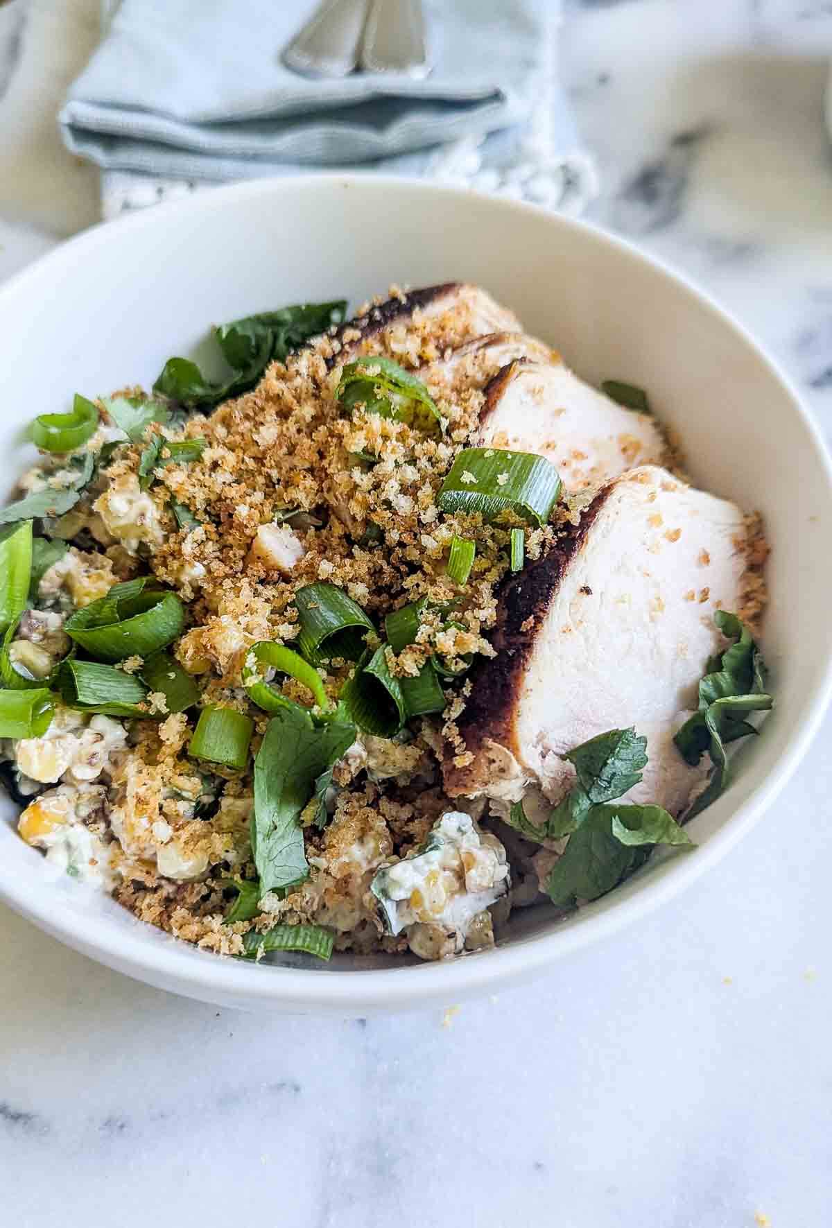 a street corn chicken and rice bowl on a marlble countertop with cilantro and lime on the side.