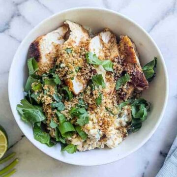 a bowl of rice, chicken, street corn and toppings on a marble surface.