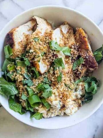 a bowl of rice, chicken, street corn and toppings on a marble surface.