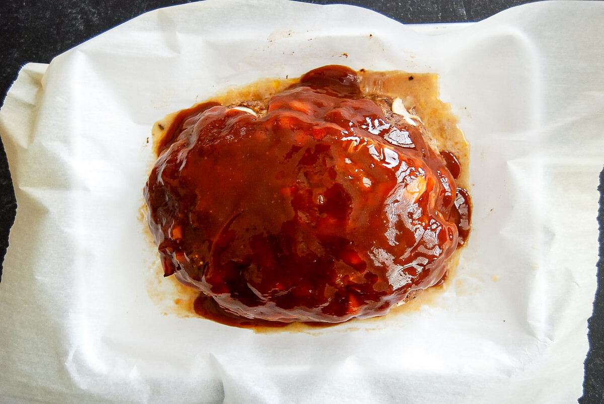 A cooked meatloaf covered in a glossy meatloaf sauce sits on a sheet of white parchment paper.