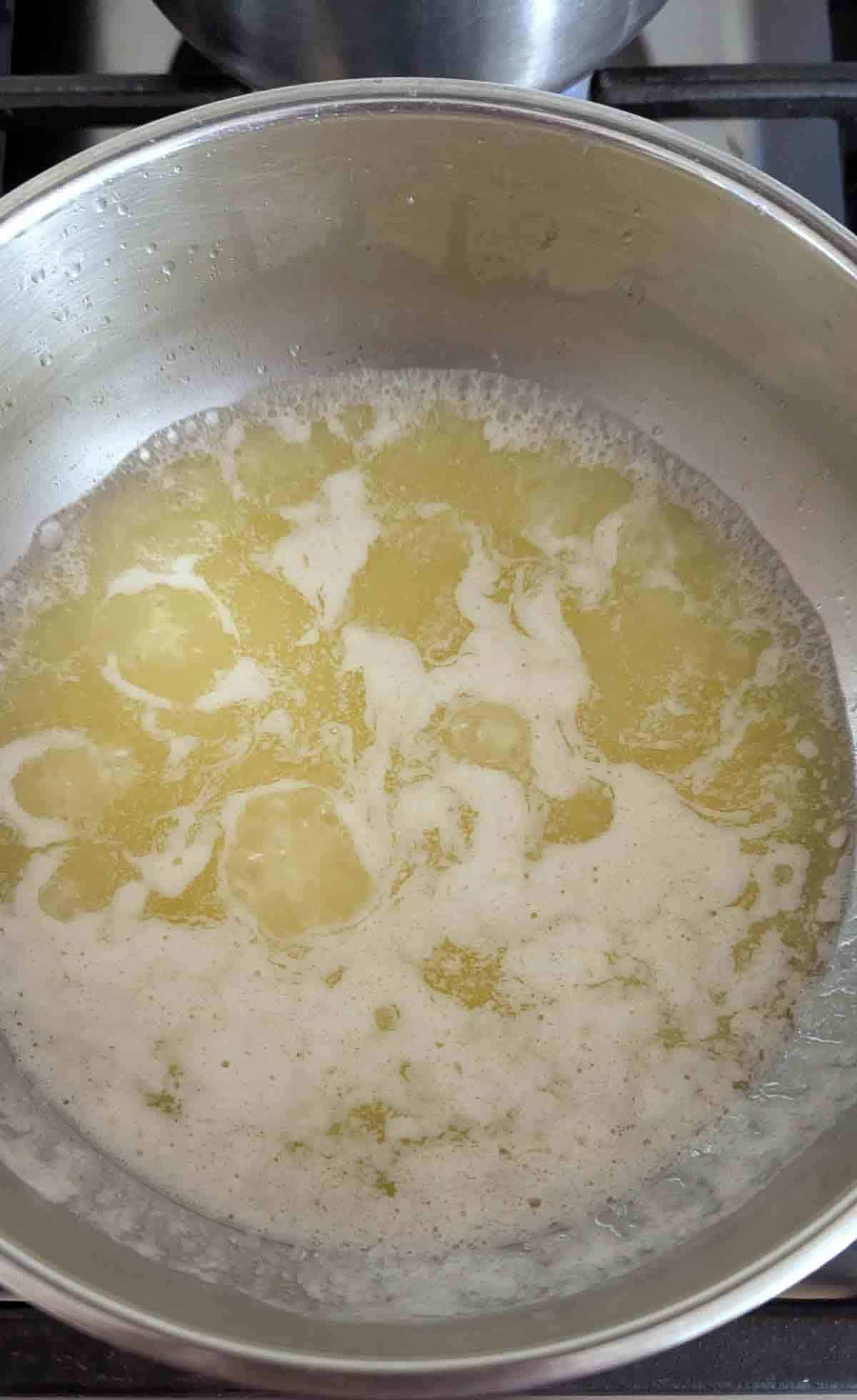 Melted butter foaming and bubbling in a stainless steel pan on a stovetop