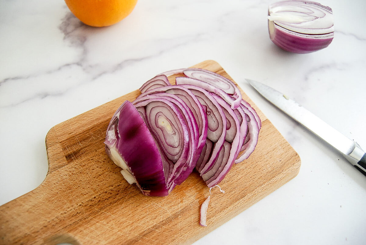 Sliced red onion on a wooden cutting board with a knife nearby.