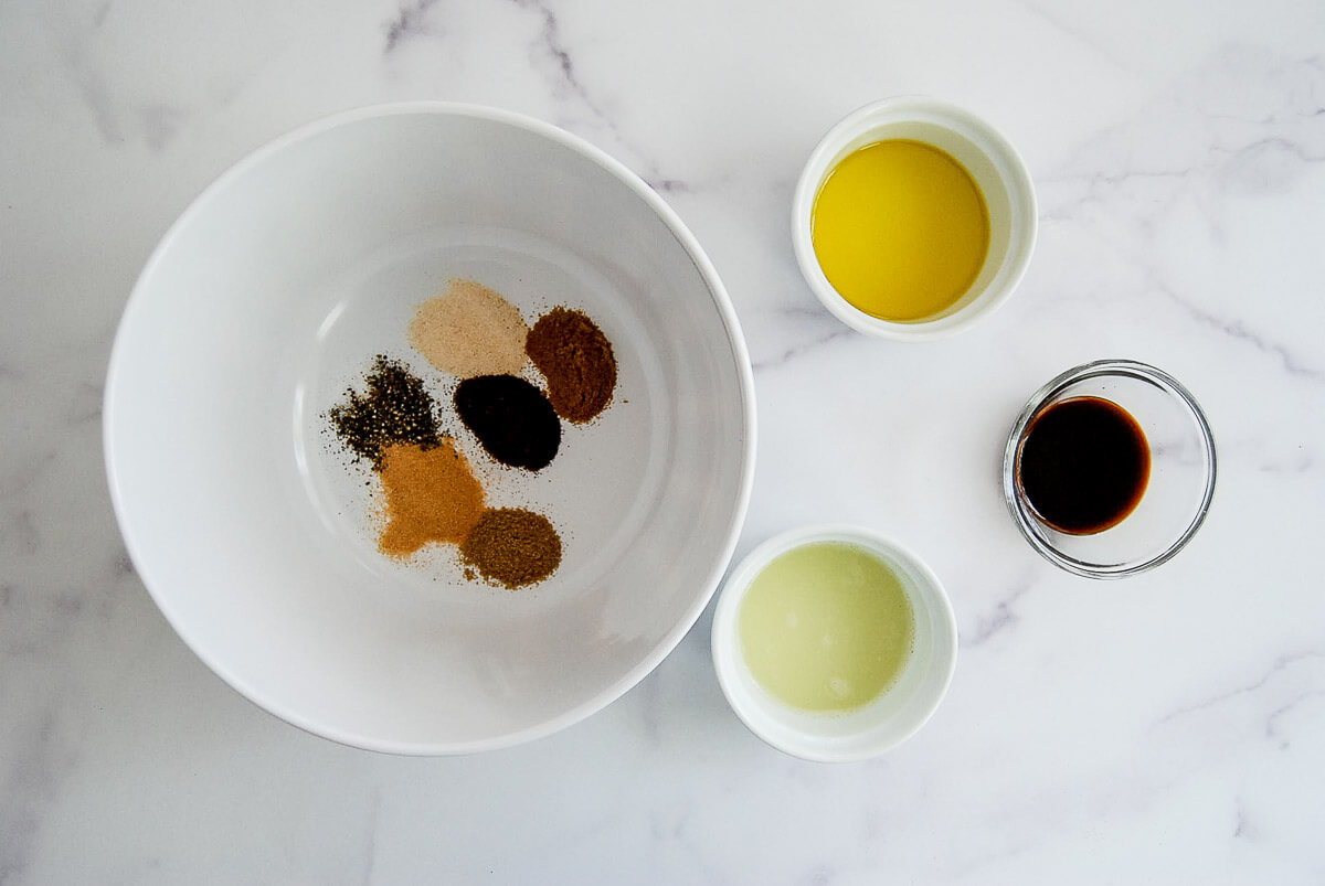 Spices for skirt steak marinade in a bowl with oil, lime juice and Worcestershire sauce next to it.