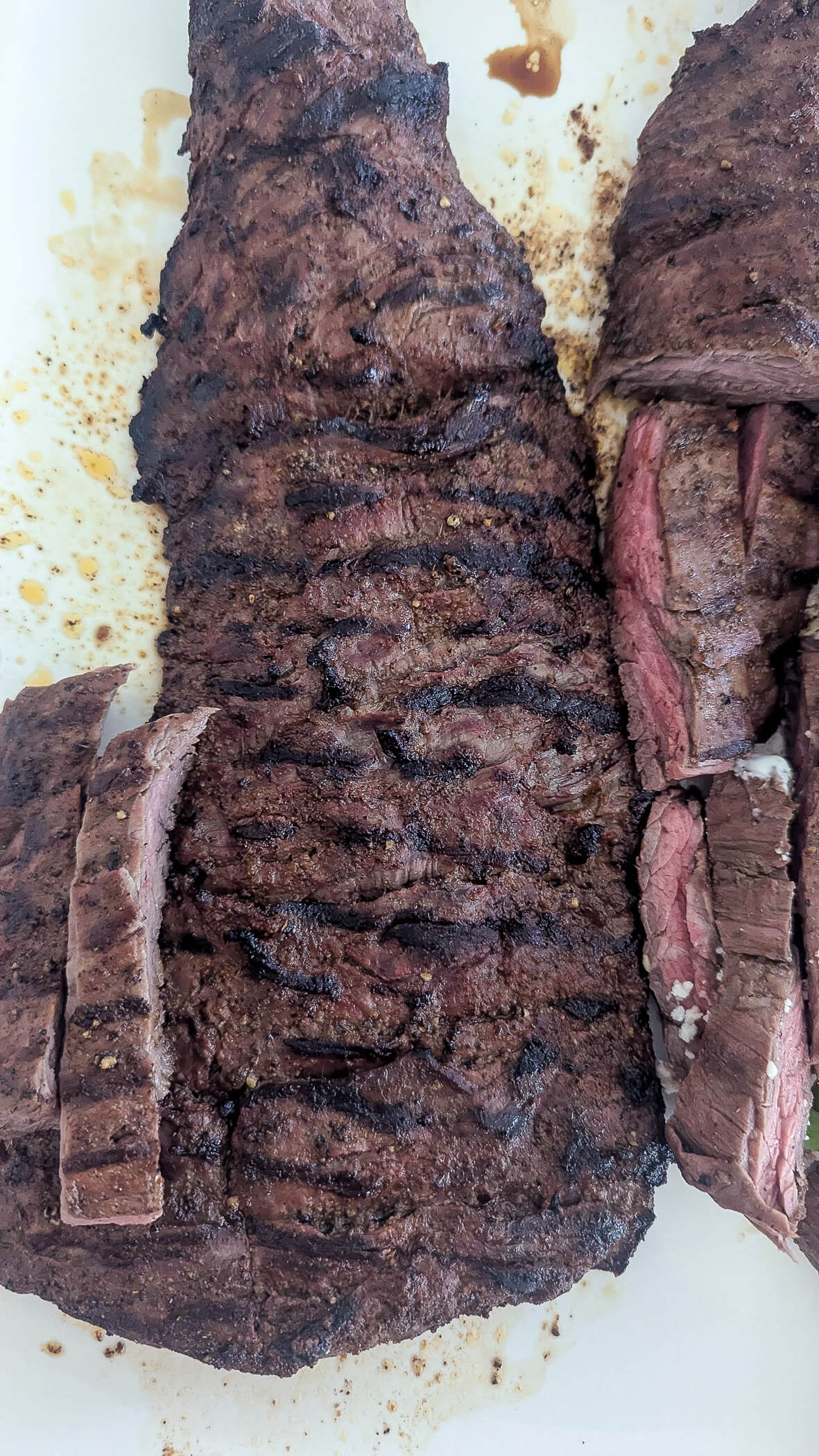 Grilled skirt steak with char marks, partially sliced against the grain to reveal a juicy, medium-rare interior on a white surface.