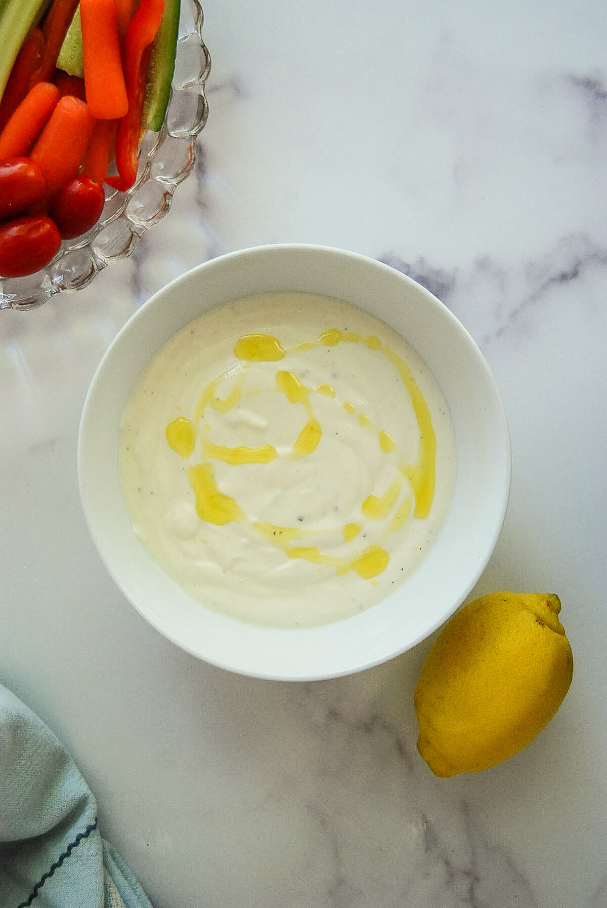 A bowl of creamy whipped feta dip drizzled with olive oil sits next to a lemon.