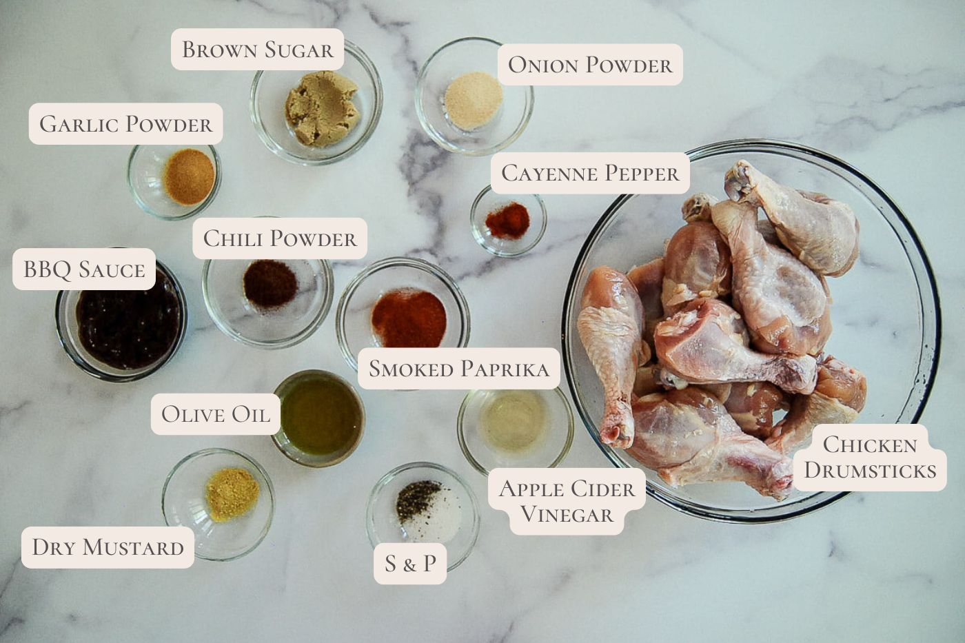 A bowl of raw chicken drumsticks surrounded by small bowls containing BBQ sauce, spices, brown sugar, olive oil, and vinegar, each labeled with their name.