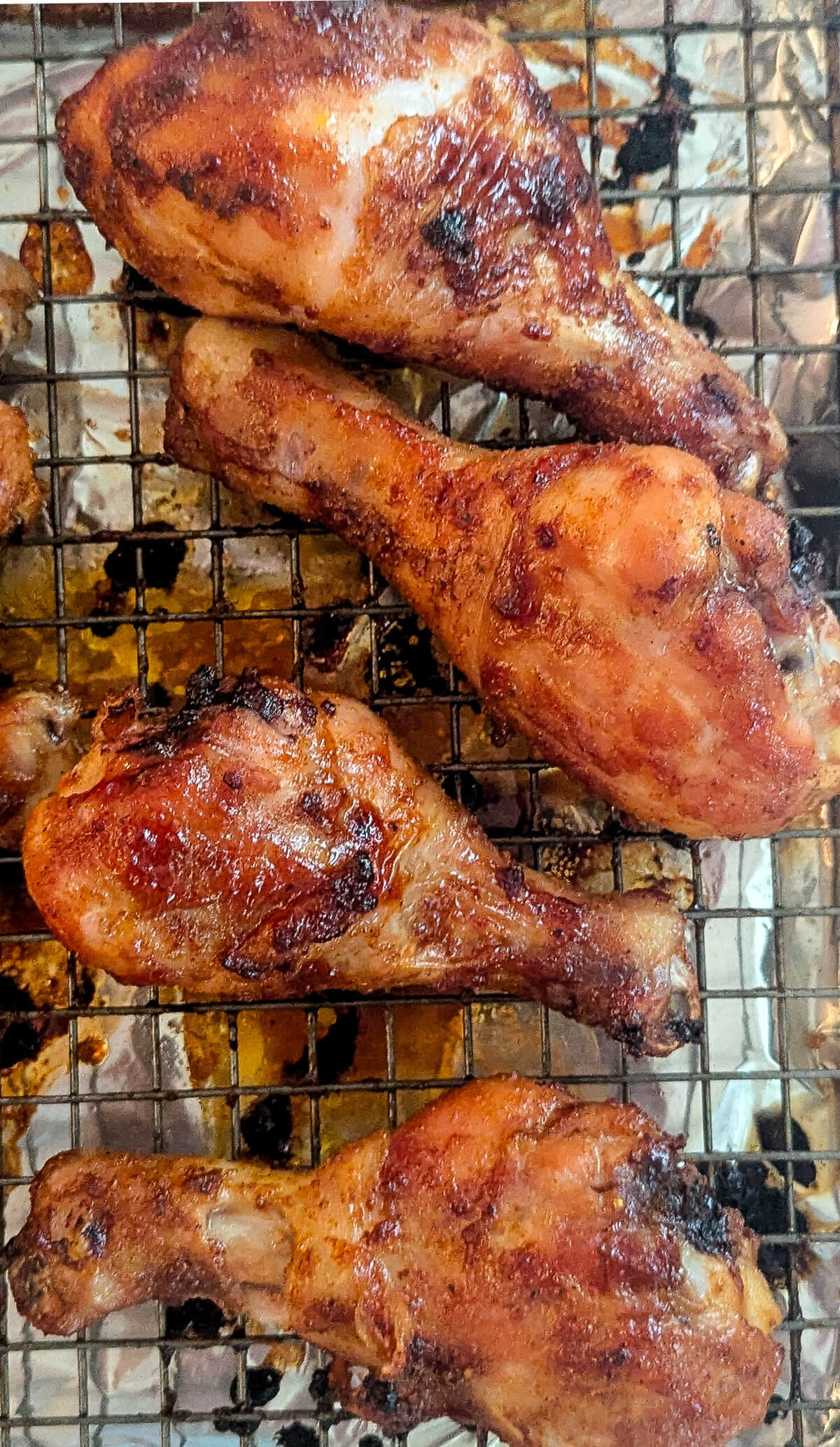 Four cooked, golden-brown bbq chicken drumsticks on a wire rack.