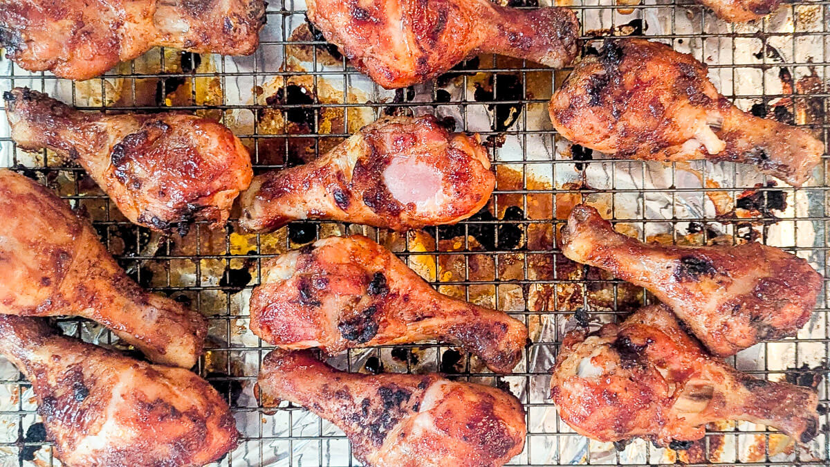 Oven baked barbecue chicken drumsticks with crispy skin on a metal rack.