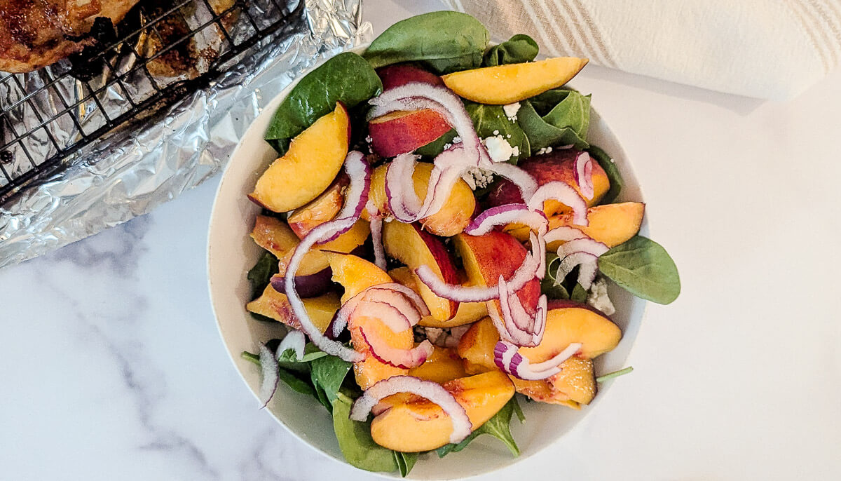 A bowl of fresh spinach salad topped with sliced peaches and red onions.