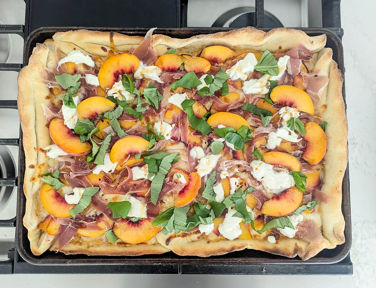 Rectangular pizza topped with peach slices, prosciutto, torn burrata, and fresh basil.