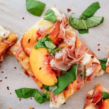 A square slice of peach pizza topped with prosciutto, peach slices, fresh basil leaves, and melted cheese, garnished with red pepper flakes.
