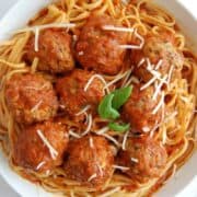 A plate of spaghetti topped with tomato sauce, baked turkey meatballs, grated cheese, and a small basil garnish in the center.