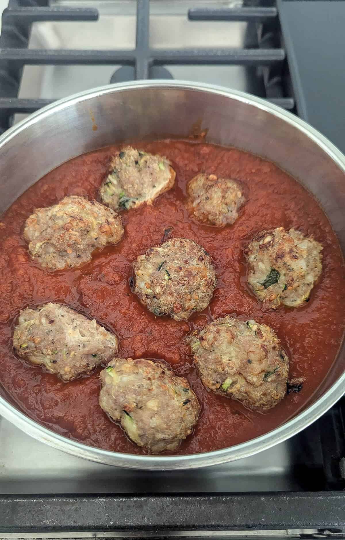 A pot of turkey meatballs sitting in tomato sauce on a stove with a metal grate, ready to be served.