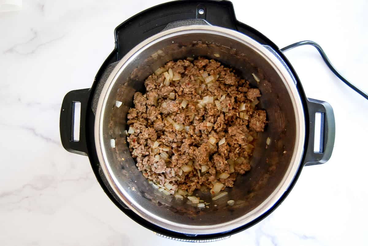 Ground beef and chopped onions are cooking inside an open crockpot on a white countertop.