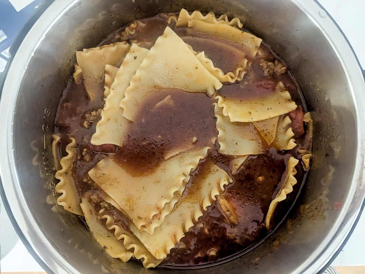 A pot filled with uncooked lasagna noodles layered over a mixture of ground meat, tomato sauce, and broth, as the ingredients cook together.