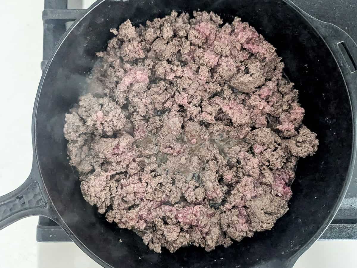 Ground meat browning in a cast iron skillet on a stovetop.